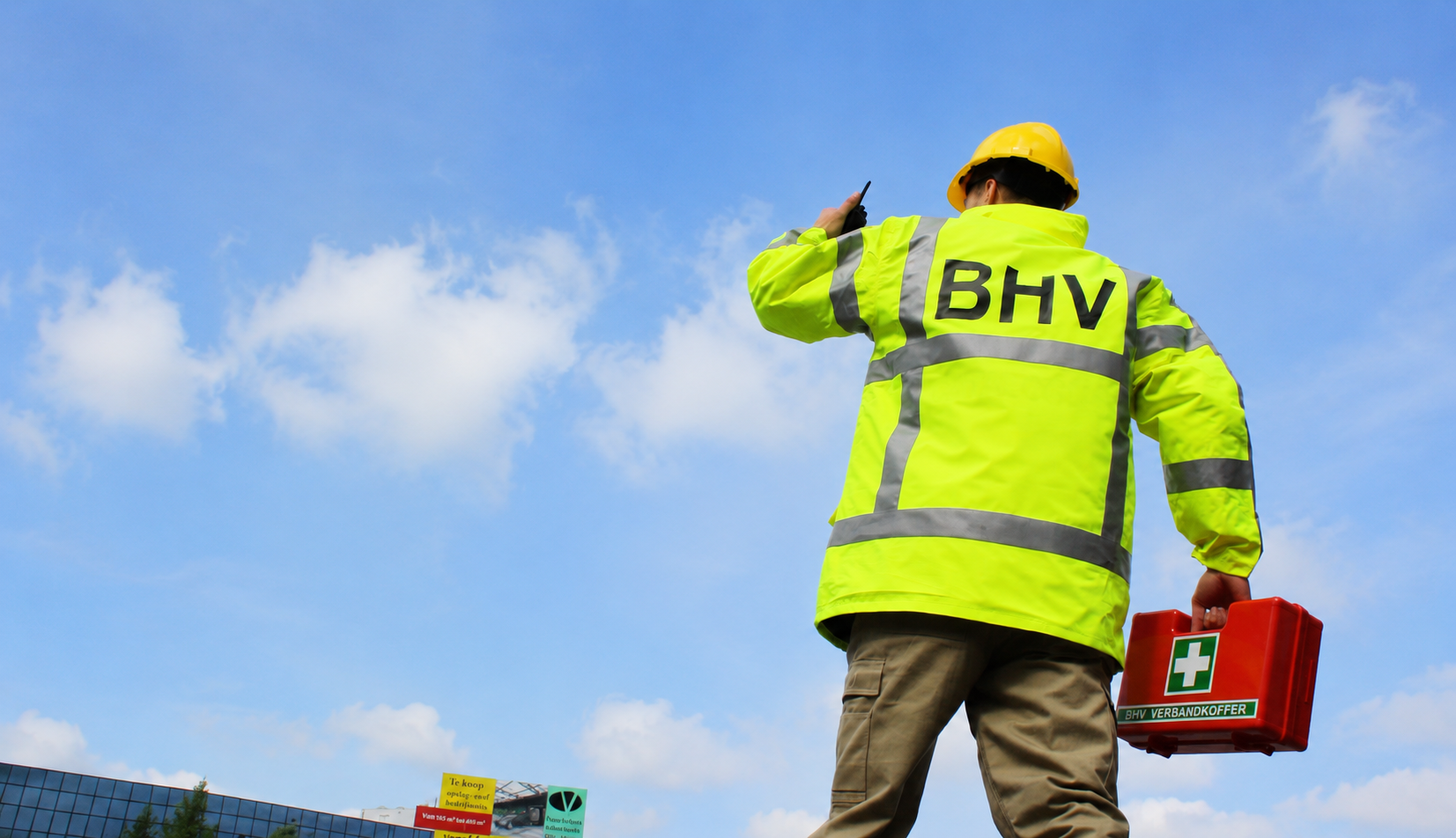 BHV-coördinator kijkt uit over het bedrijfsterrein met een verbandkoffer